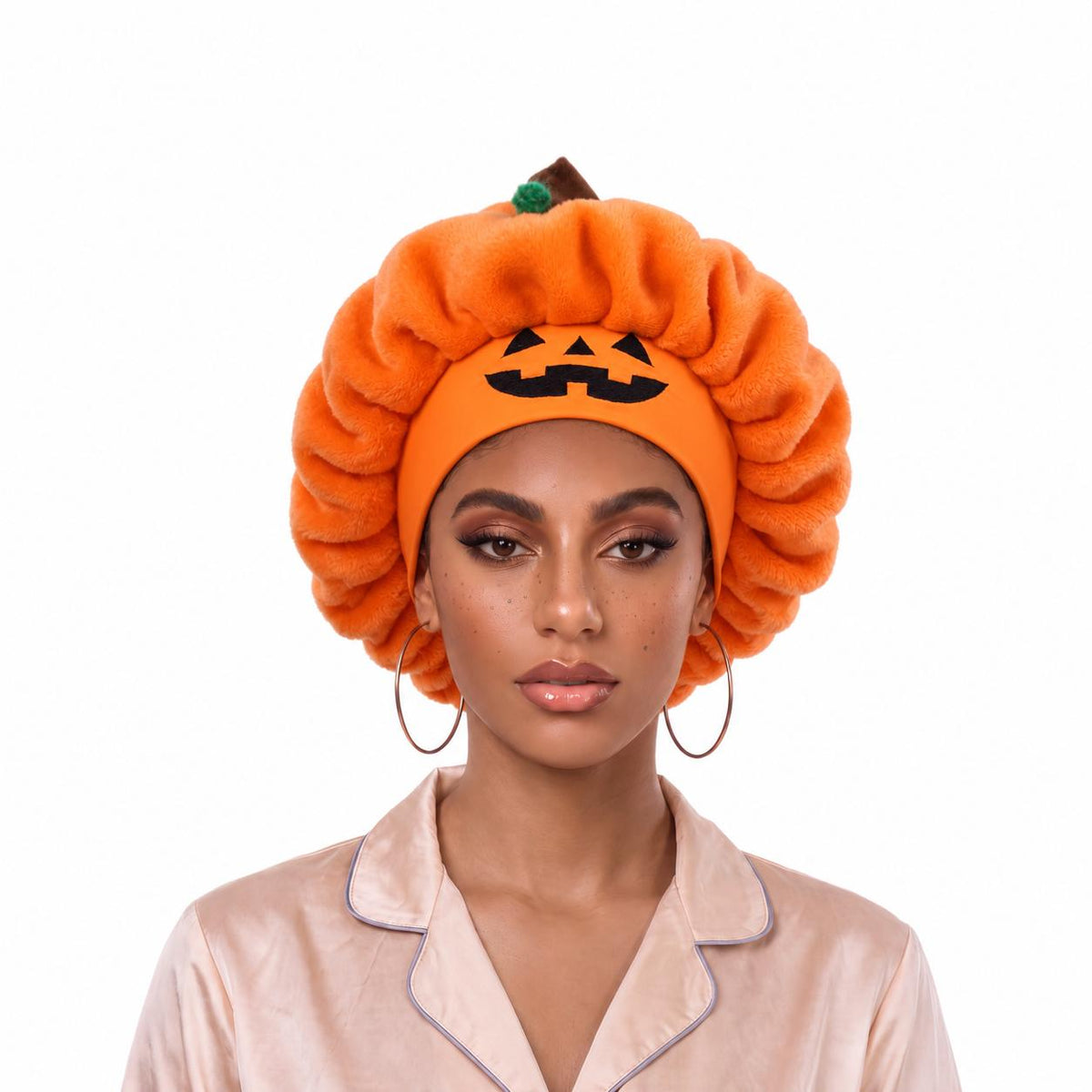 Orange plush pumpkin sleep cap worn on a model, jack-o'-lantern face at the front